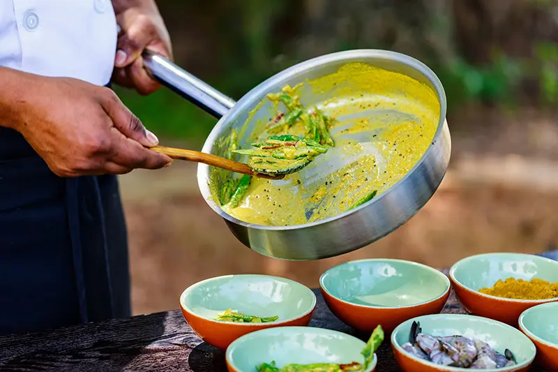 Gerichte werden aus einer Pfanne in Schüsseln portioniert